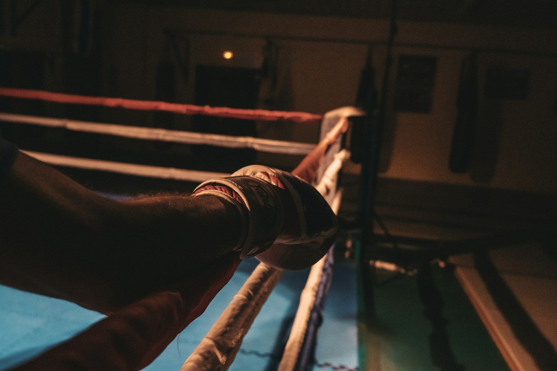 Boxer's wrapped hand on dimly lit ring ropes.