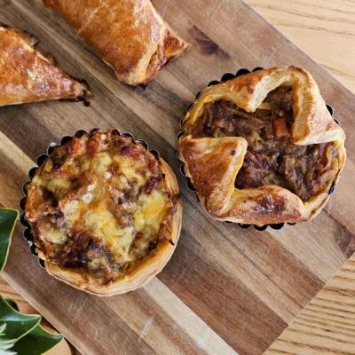Four golden-brown savory pastries, including two tarts, a roll, and a turnover, on a wooden board. Four golden-brown savory pastries, including two tarts, a roll, and a turnover, on a wooden board.