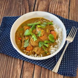 a bowl of curry with rice and vegetables on a wooden table with a fork .