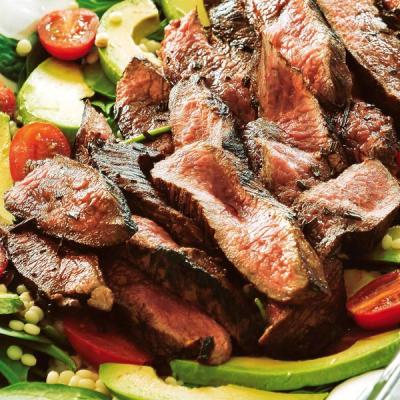 Close-up of sliced steak with avocado, cherry tomatoes, and grains.