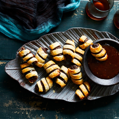 Golden-brown spiral pastries with a dark filling, served on a gray platter with a bowl of dark dipping sauce.
