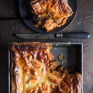 a pie with a slice taken out of it is in a pan on a wooden table . a pie with a slice taken out of it is in a pan on a wooden table .