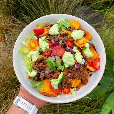 a person is holding a bowl of nachos with guacamole and tomatoes, beef and kumara. a person is holding a bowl of nachos with guacamole and tomatoes, beef and kumara.