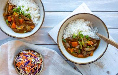 two bowls of beef curry with rice and a bowl of coleslaw on a table . two bowls of beef curry with rice and a bowl of coleslaw on a table .