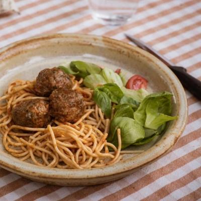 A plate of spaghetti with three meatballs and a side salad on a striped tablecloth.