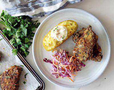 A plate with breaded cutlets, a loaded baked potato, and coleslaw salad.
