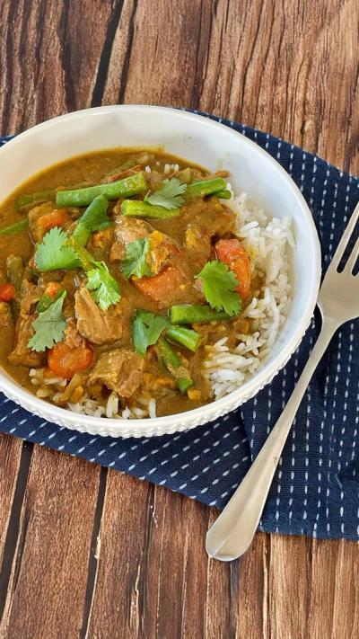 a bowl of curry with rice and a fork on a wooden table .