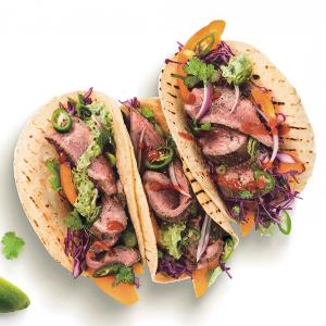 three tacos with meat , vegetables and guacamole on a white background .