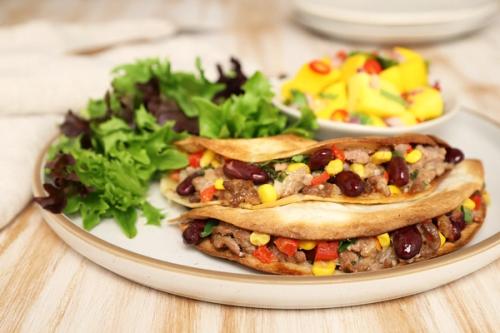 a close up of a plate of food with lamb and bean buritos and salad a close up of a plate of food with lamb and bean buritos and salad