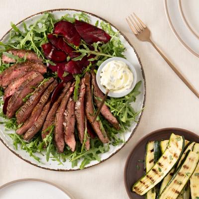A plate of sliced steak, rocket, red beets, and creamy sauce, with a side of grilled zucchini. A plate of sliced steak, rocket, red beets, and creamy sauce, with a side of grilled zucchini.