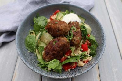 A bowl of lamb koftas with couscous, spinach, cucumber, red peppers, and yogurt.