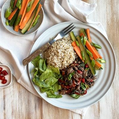A plate of ground beef0 and basil stir-fry, brown rice, fresh lettuce, and sliced carrots and cucumbers. A plate of ground beef0 and basil stir-fry, brown rice, fresh lettuce, and sliced carrots and cucumbers.