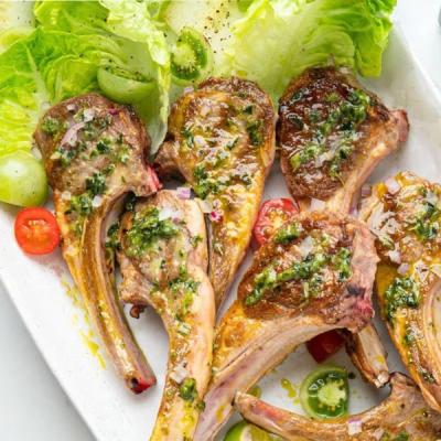 Grilled lamb chops with green sauce, lettuce, and tomatoes.