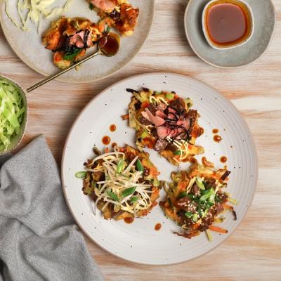 Assorted savory pancakes topped with various meats, vegetables, and sauces, served on plates.