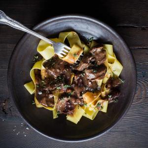 a plate of pasta with meat and sauce and a fork on a wooden table