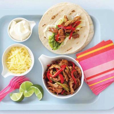 a tray with a tortilla, a bowl of meat, cheese, limes and sour cream.