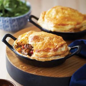two pot pies are sitting on a wooden tray on a table