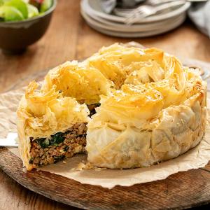 a filo pie with a slice taken out of it is on a wooden cutting board