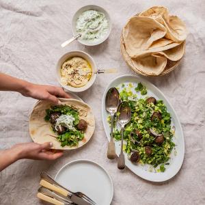a table topped with wraps, meatballs and salad with yoghurt dressing