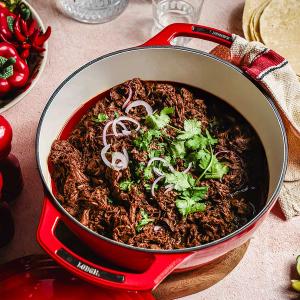 a red casserole pot filled with beef and cilantro on a table