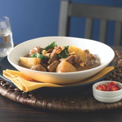 A bowl of meat and potato stew topped with greens and peanuts, with a side of chopped red chilies. A bowl of meat and potato stew topped with greens and peanuts, with a side of chopped red chilies.