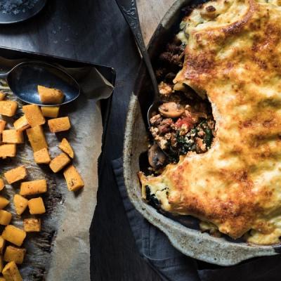 Golden-crusted casserole with a scoop removed, revealing savory filling, beside roasted butternut squash. Golden-crusted casserole with a scoop removed, revealing savory filling, beside roasted butternut squash.
