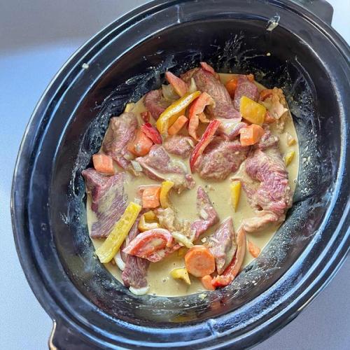 a crock pot filled with meat and vegetables is sitting on a table . a crock pot filled with meat and vegetables is sitting on a table .