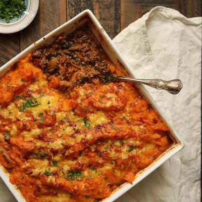 A white baking dish of sweet potato-topped cottage pie, partially scooped with a spoon. A white baking dish of sweet potato-topped cottage pie, partially scooped with a spoon.