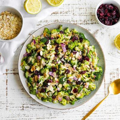 a plate of broccoli salad with almonds , cranberries and onions on a table . a plate of broccoli salad with almonds , cranberries and onions on a table .
