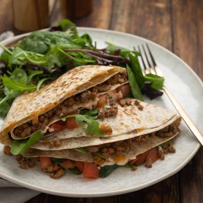A platter of beef mince with tomatoes, and greens, served with a side salad and pita breads. 