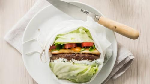 A lettuce-wrapped burger with tomato and cheese on a white plate, next to a knife.