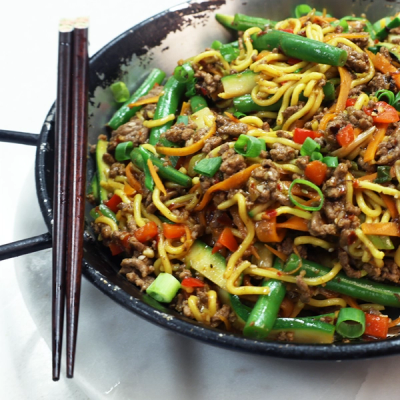 a wok filled with noodles meat and vegetables with chopsticks in it a wok filled with noodles meat and vegetables with chopsticks in it