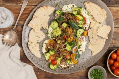 A large platter with seasoned lamb meat, cucumber and tomato salad, creamy white dip, and pita bread. A large platter with seasoned lamb meat, cucumber and tomato salad, creamy white dip, and pita bread.