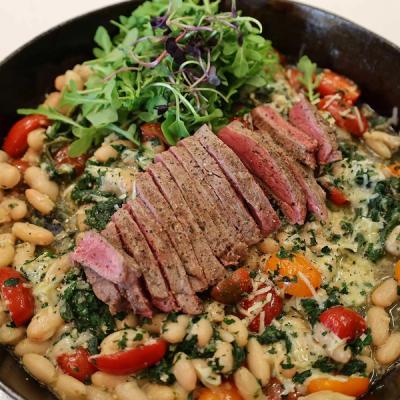 a skillet filled with beans , tomatoes , spinach and slliced steak . a skillet filled with beans , tomatoes , spinach and slliced steak .