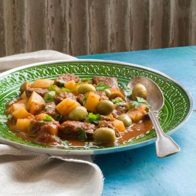 Stew of meat, potatoes, and green olives with parsley, served on a green plate with a spoon. Stew of meat, potatoes, and green olives with parsley, served on a green plate with a spoon.