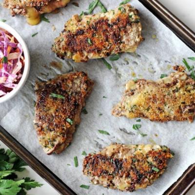 Golden-brown breaded cutlets with herbs on a baking sheet, with a side of coleslaw.