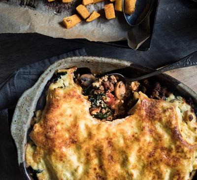 a casserole dish with a spoon in it next to a pan of roasted butternut squash . a casserole dish with a spoon in it next to a pan of roasted butternut squash .