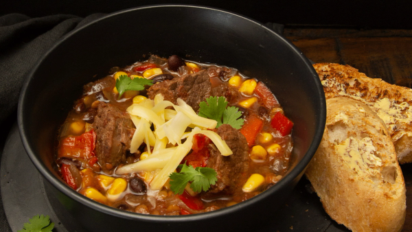 a bowl of chili with cheese and bread on the side