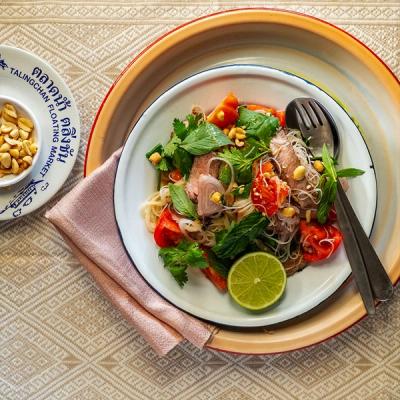 a plate of Thai beef salad with tomato with a fork and spoon on a table