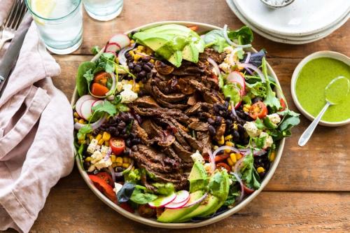 a plate of food on a table with a beef and avocado salad on it and a green sauce on the side. a plate of food on a table with a beef and avocado salad on it and a green sauce on the side.