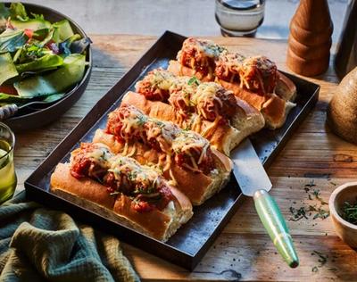 a tray of hot dogs with meatballs and cheese on a wooden table . a tray of hot dogs with meatballs and cheese on a wooden table .