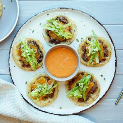 a white plate topped with smashed dumplings with lettuce and sauce on top and a bowl of dipping sauce .