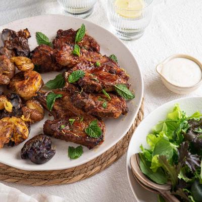 a white plate topped with meat and potatoes on a table next to a bowl of salad.