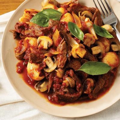 A plate of shell pasta with beef, mushrooms, and onions in tomato sauce, garnished with basil. A plate of shell pasta with beef, mushrooms, and onions in tomato sauce, garnished with basil.