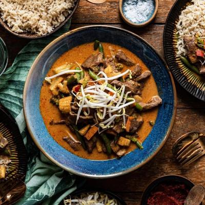 A large bowl of beef and vegetable curry topped with bean sprouts, served with brown rice.