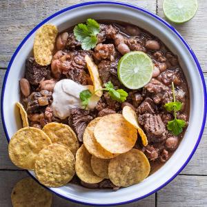 a bowl of beef with tortilla chips and sour cream on a wooden table