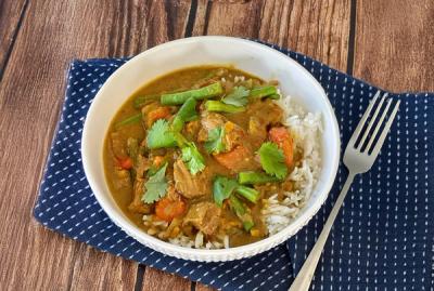 a bowl of curry with rice and a fork on a wooden table .