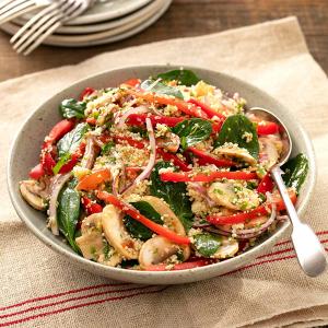 a bowl of salad with spinach , mushrooms , red peppers , onions and couscous on a table .