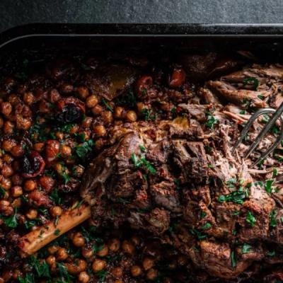 Tender roasted lamb leg with chickpeas and herbs, being shredded with a fork in a pan. Tender roasted lamb leg with chickpeas and herbs, being shredded with a fork in a pan.