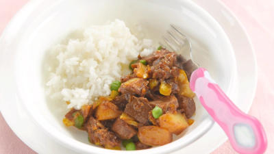 A bowl of white rice and meat stew with potatoes and peas, with a pink child's fork. A bowl of white rice and meat stew with potatoes and peas, with a pink child's fork.